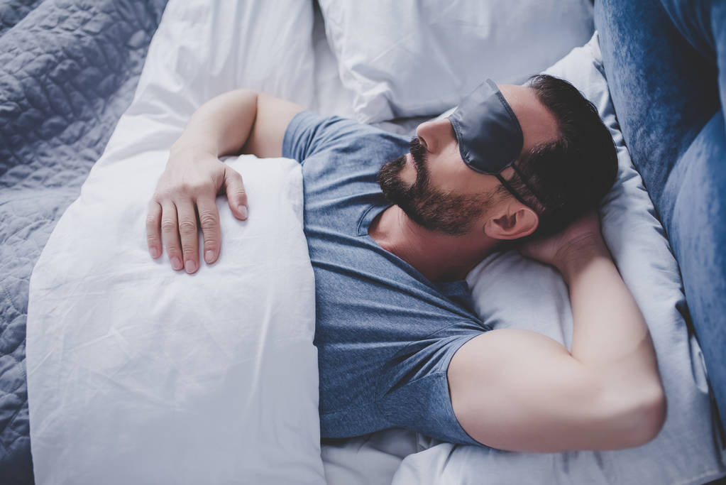 Портрет красивого чоловіка у сплячій масці лежить у ліжку
 - Фото, зображення