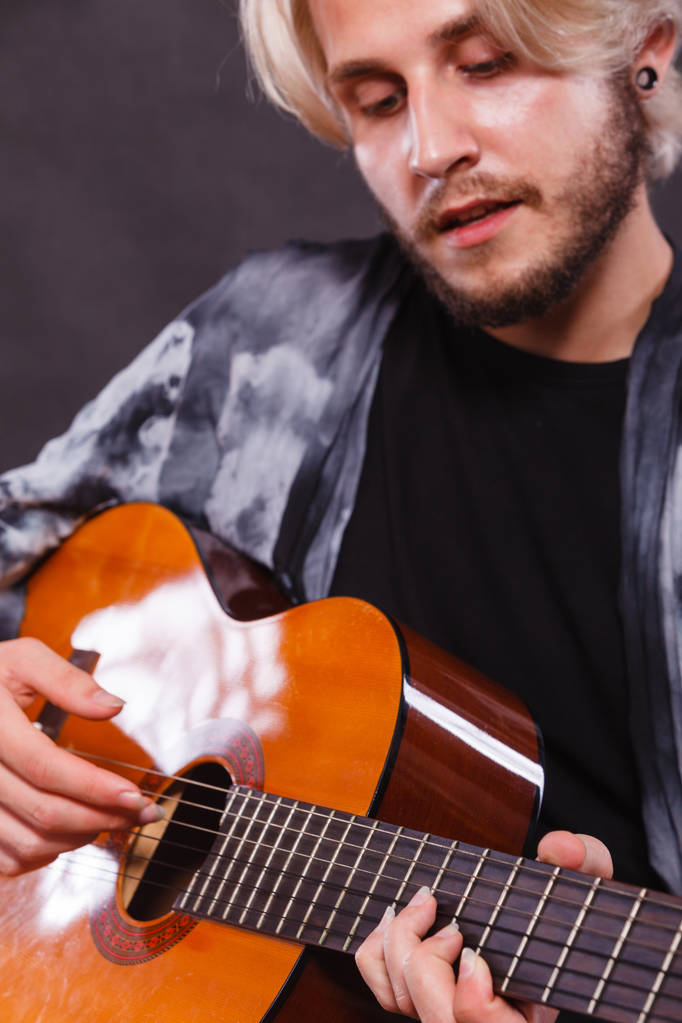 Musik, Leidenschaft. junger blonder Mann in schickem Hemd, der auf akustischer Gitarre spielt und singt, Studioaufnahme, schwarzer Hintergrund. - Foto, Bild