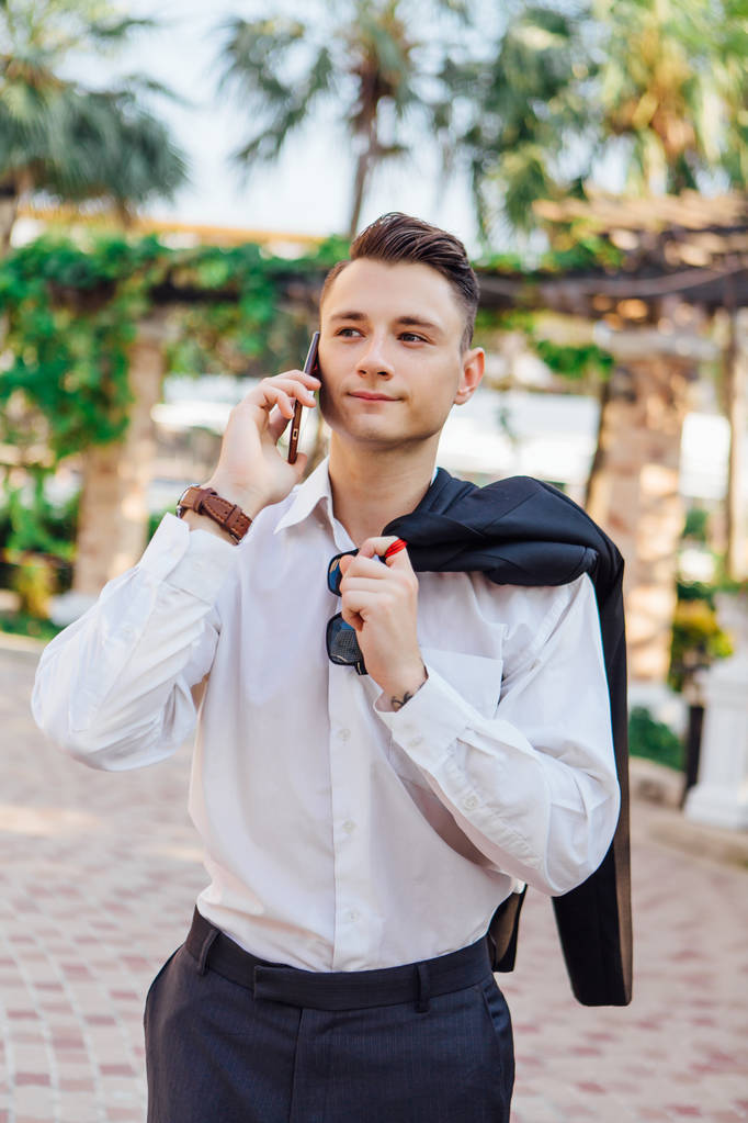 Νεαρός επιχειρηματίας, μιλώντας στο τηλέφωνό του σε εξωτερικούς χώρους σε μια τροπική χώρα - Φωτογραφία, εικόνα