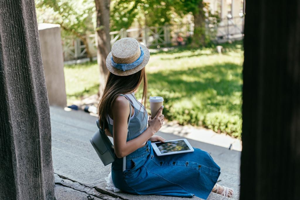вибірковий фокус молодої жінки, що тримає паперову чашку і використовує цифровий планшет, сидячи на сходах
 - Фото, зображення