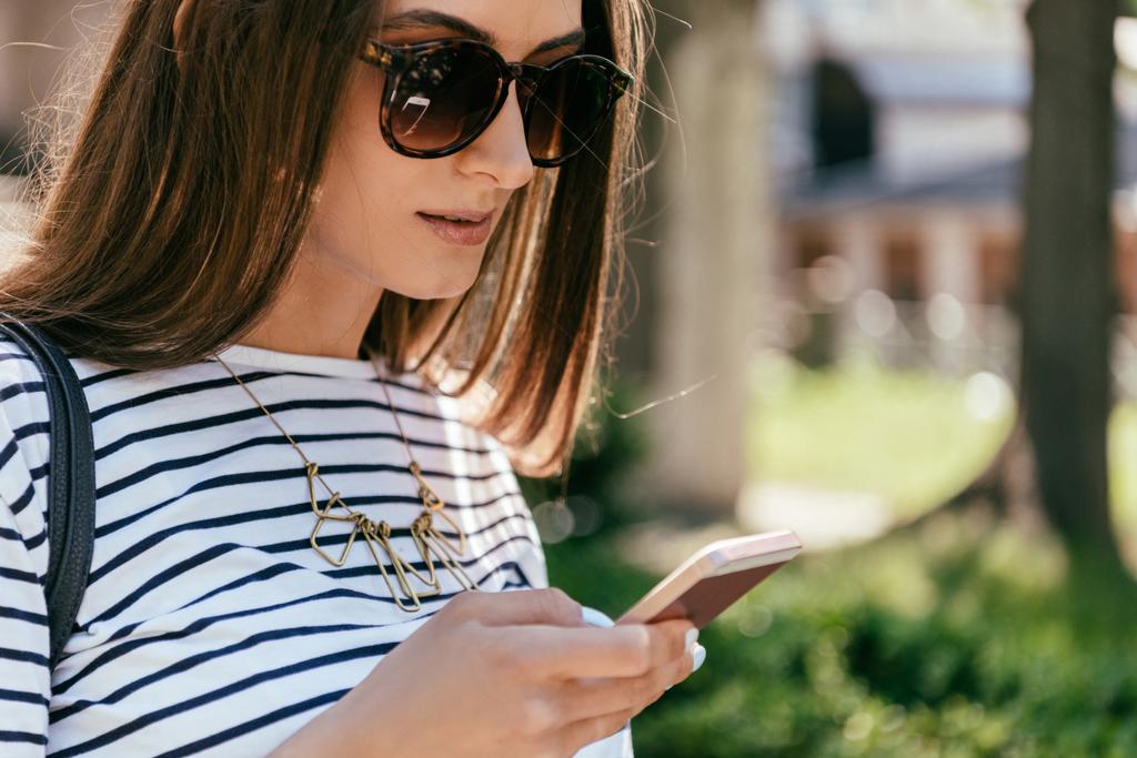 Nahaufnahme eines schönen Mädchens mit Sonnenbrille mit Smartphone auf der Straße - Foto, Bild