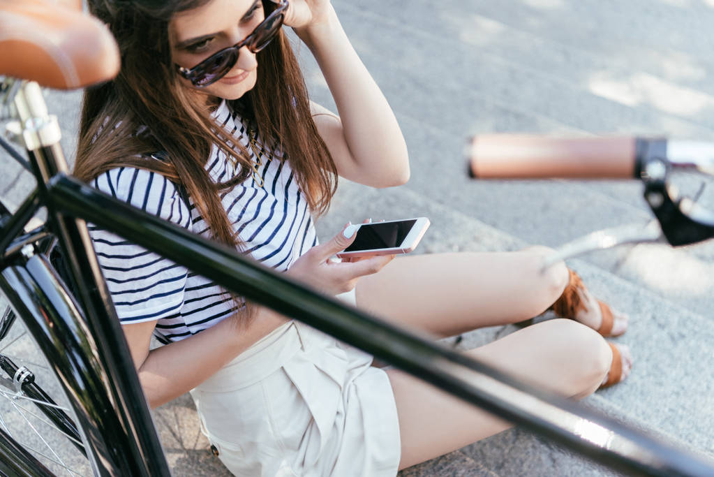 hoge hoekmening van meisje in zonnebril zittend op de trap en het gebruik van smartphone - Foto, afbeelding