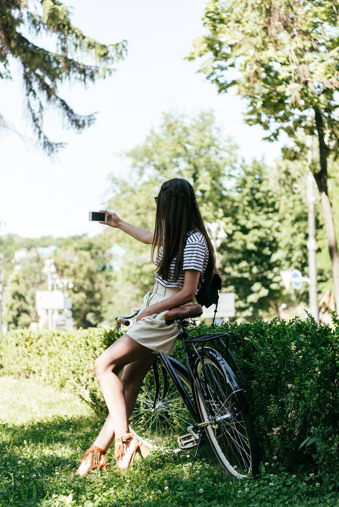 привлекательная девушка сидит на велосипеде и делает селфи со смартфоном на улице
 - Фото, изображение