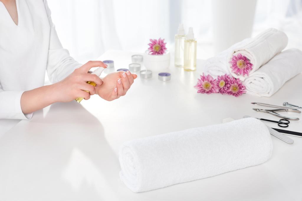 przycięty obraz kobiety za pomocą oleju zapach przy stole z ręcznikami, kwiaty, świece i przyrządy do manicure w salonie piękności - Zdjęcie, obraz