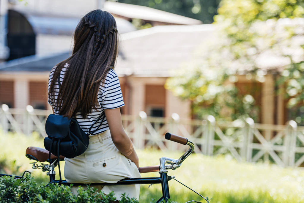 πίσω όψη της γυναίκας με πακέτο πίσω κλίνει σε ρετρό ποδήλατο στο πάρκο - Φωτογραφία, εικόνα