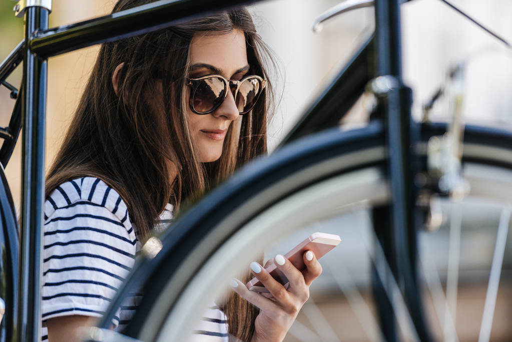 retrato de mujer joven usando un teléfono inteligente mientras está sentada cerca de la bicicleta retro en la calle
 - Foto, imagen
