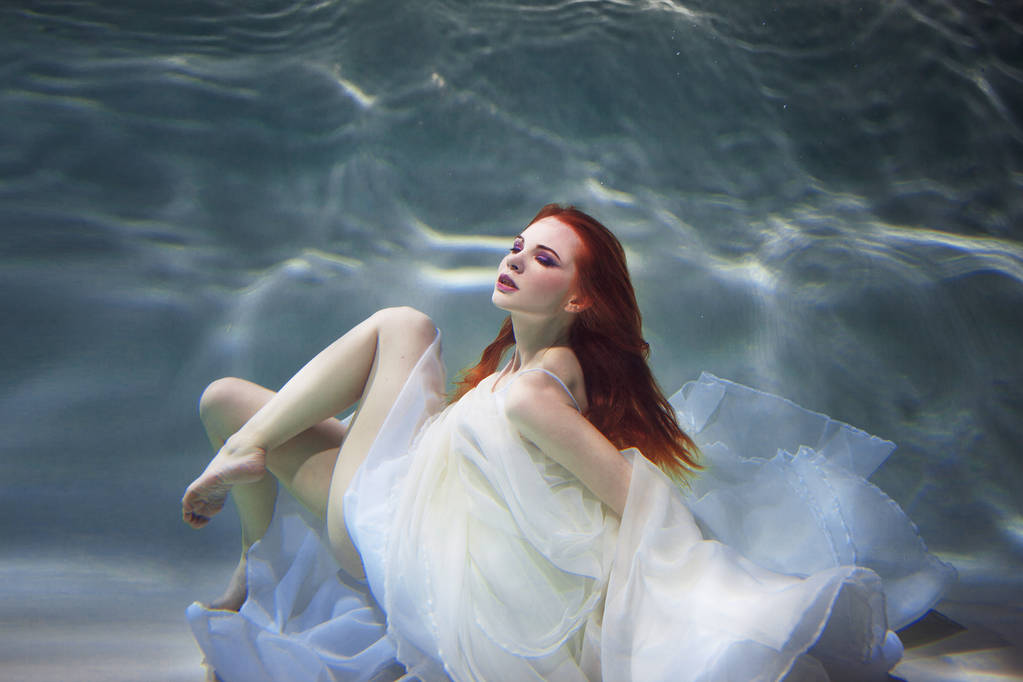 Подводная девушка. Красивая рыжая женщина в белом платье, плавающая под водой
. - Фото, изображение