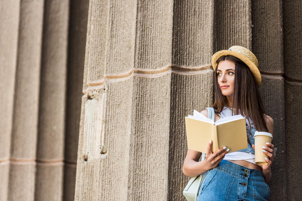 portrait of pretty young woman with opened book and coffee to go on street - Photo, Image