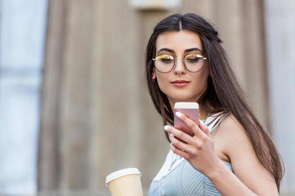 Porträt einer jungen Frau mit Brille und Kaffee zum Smartphone auf der Straße - Foto, Bild