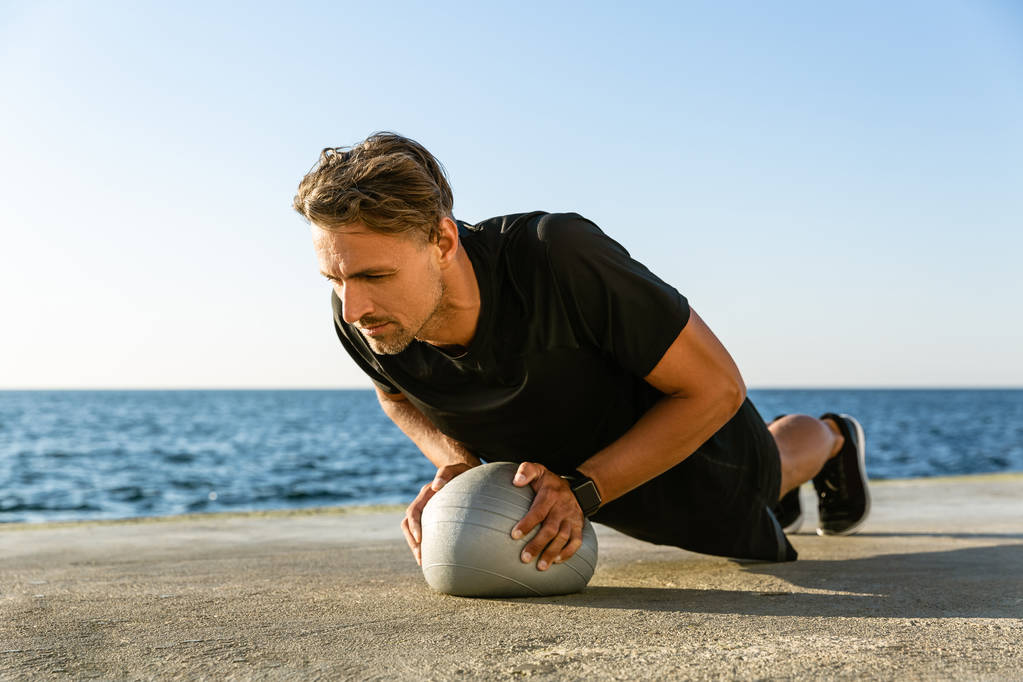 komea aikuinen urheilija tekee push ups sopii pallo meren rannalla
 - Valokuva, kuva