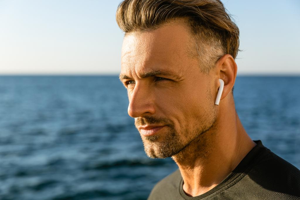 portrait en gros plan d'un homme adulte attrayant avec écouteurs sans fil sur le bord de la mer
 - Photo, image