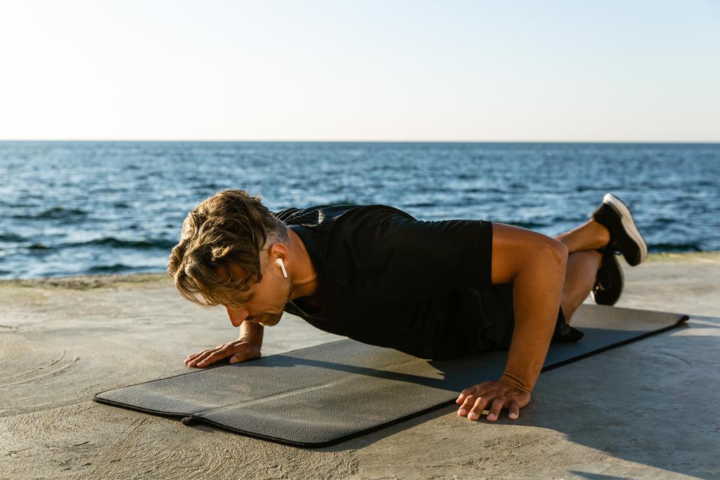 pro dospělé sportovce s bezdrátové sluchátka dělá push up na moře - Fotografie, Obrázek