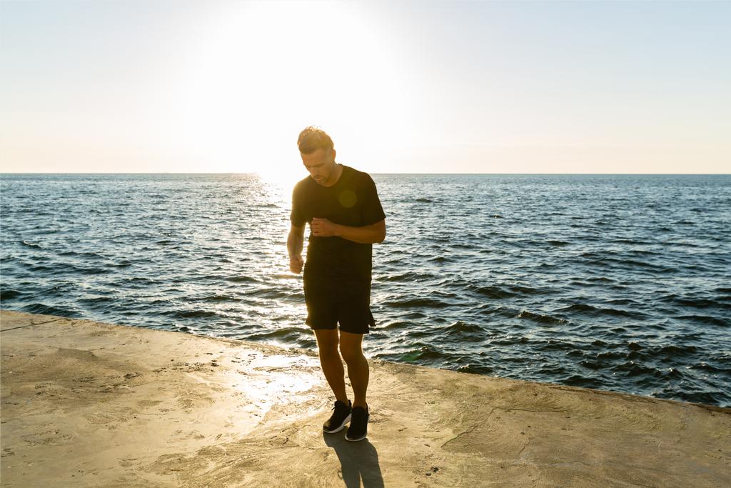 handsome adult sportsman working out on seashore in front of sunrise - Photo, Image
