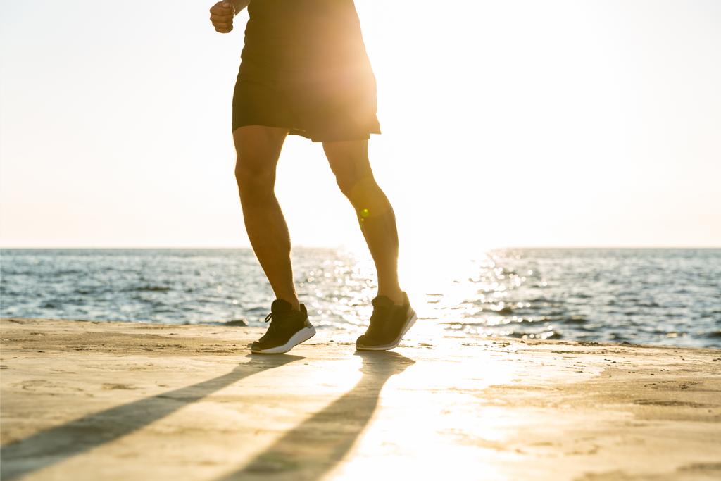 colpo ritagliato di uomo in forma che fa jogging sulla riva del mare di fronte all'alba
 - Foto, immagini