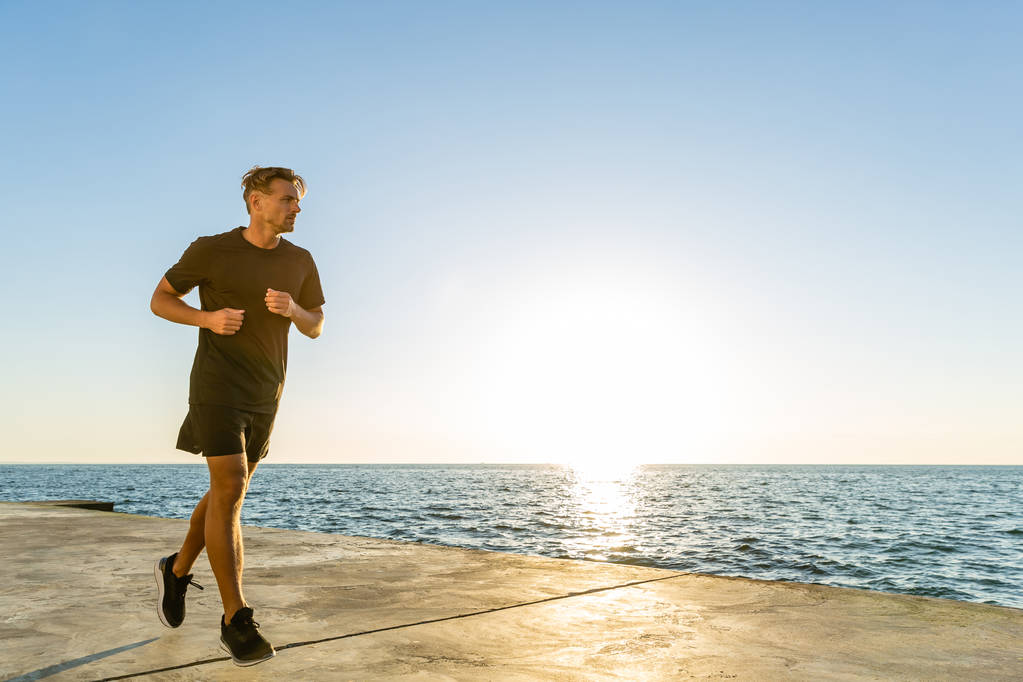 przystojny sportowiec dorosły jogging na seashore przed wschodem słońca - Zdjęcie, obraz