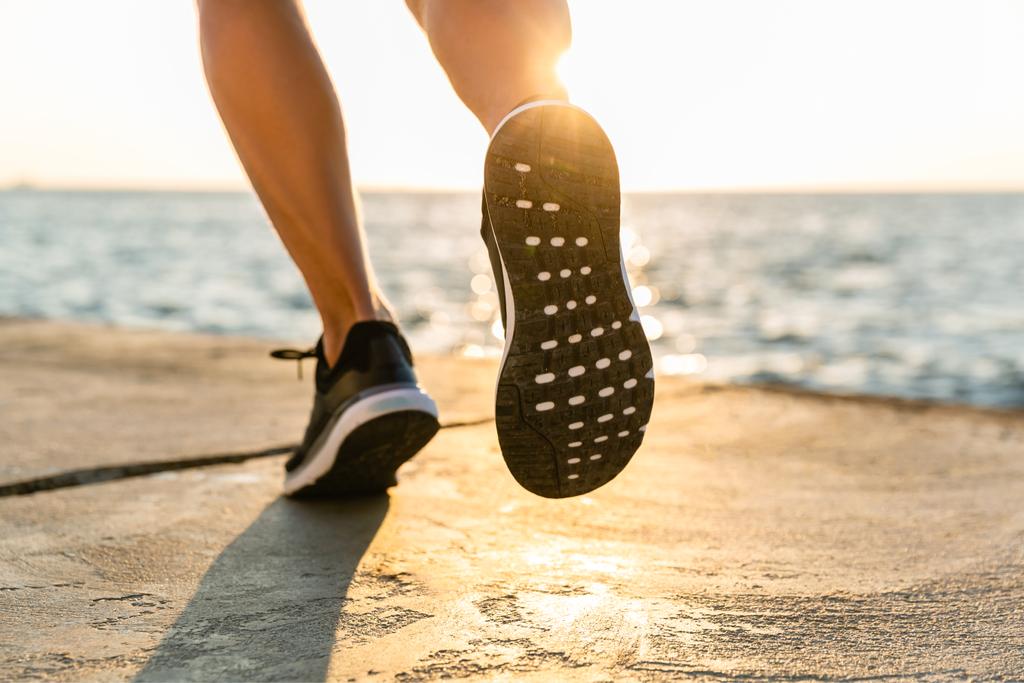 colpo ritagliato di sportivo in scarpe da ginnastica in esecuzione in riva al mare in senrise
 - Foto, immagini