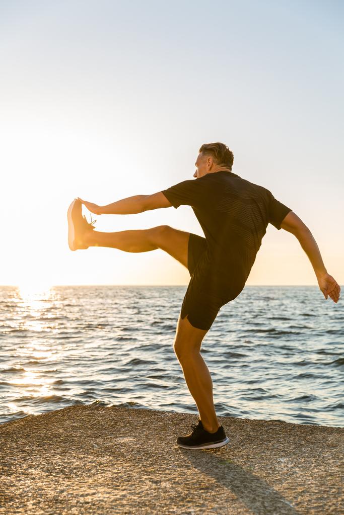 handsome adult sportsman working out on seashore in evening - Photo, Image