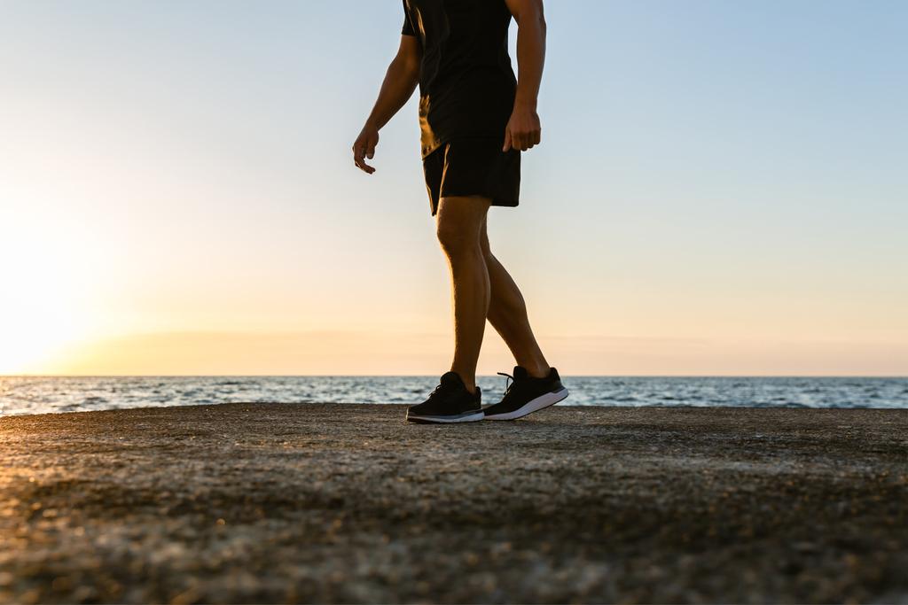 ritagliato colpo di uomo in abbigliamento sportivo moderno in piedi sulla riva del mare
 - Foto, immagini