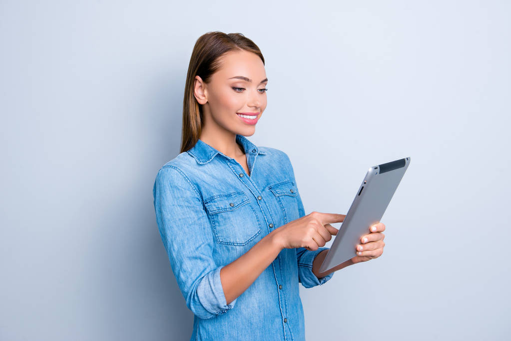 Portret van moderne drukke meisje met tablet in handen controleren van e-mail in sociale netwerken te chatten met vrienden met behulp van wifi internet geïsoleerd op een grijze achtergrond - Foto, afbeelding