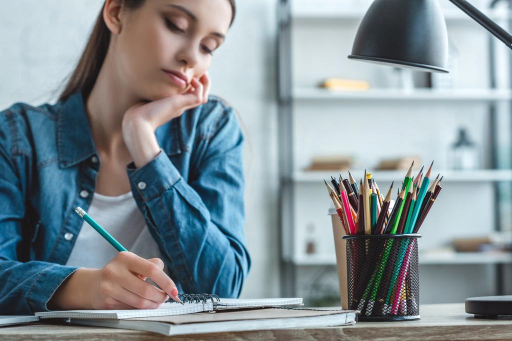 abgeschnittene Aufnahme eines gelangweilten Mädchens, das in Notizbuch schreibt und zu Hause studiert - Foto, Bild