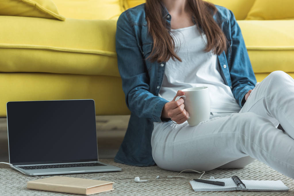 cropped shot of girl holding cup while sitting on carpet and studying at home - Photo, Image