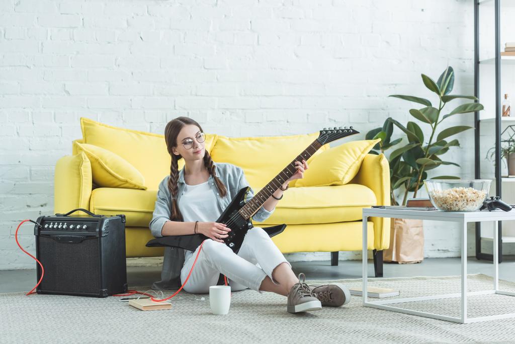 жіночий підліток музикант грає на електрогітарі на підлозі у вітальні
 - Фото, зображення