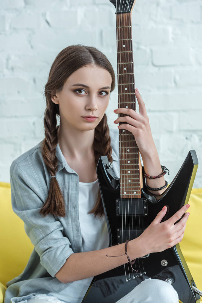 attractive teen musician with electric guitar sitting on sofa  - Photo, Image