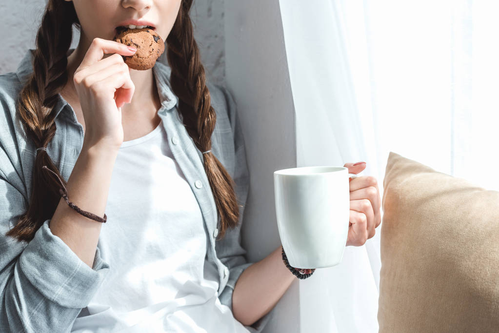 クッキーを食べ、コーヒーを飲む女の子のビューをトリミング - 写真・画像