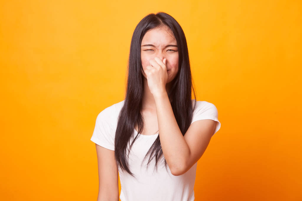 Giovane donna asiatica tenendo il naso a causa di un cattivo odore su sfondo giallo brillante
 - Foto, immagini