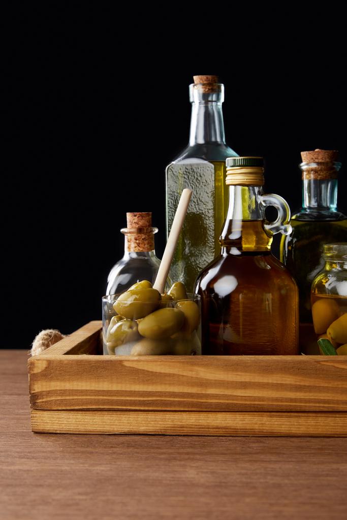diverse bottiglie di olio aromatico e vasetto con olive verdi su tavola di legno su fondo nero
 - Foto, immagini