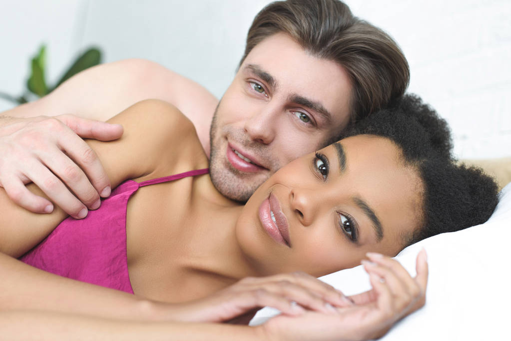 retrato de pareja joven multiétnica enamorada acostada en la cama juntos en la mañana
 - Foto, Imagen