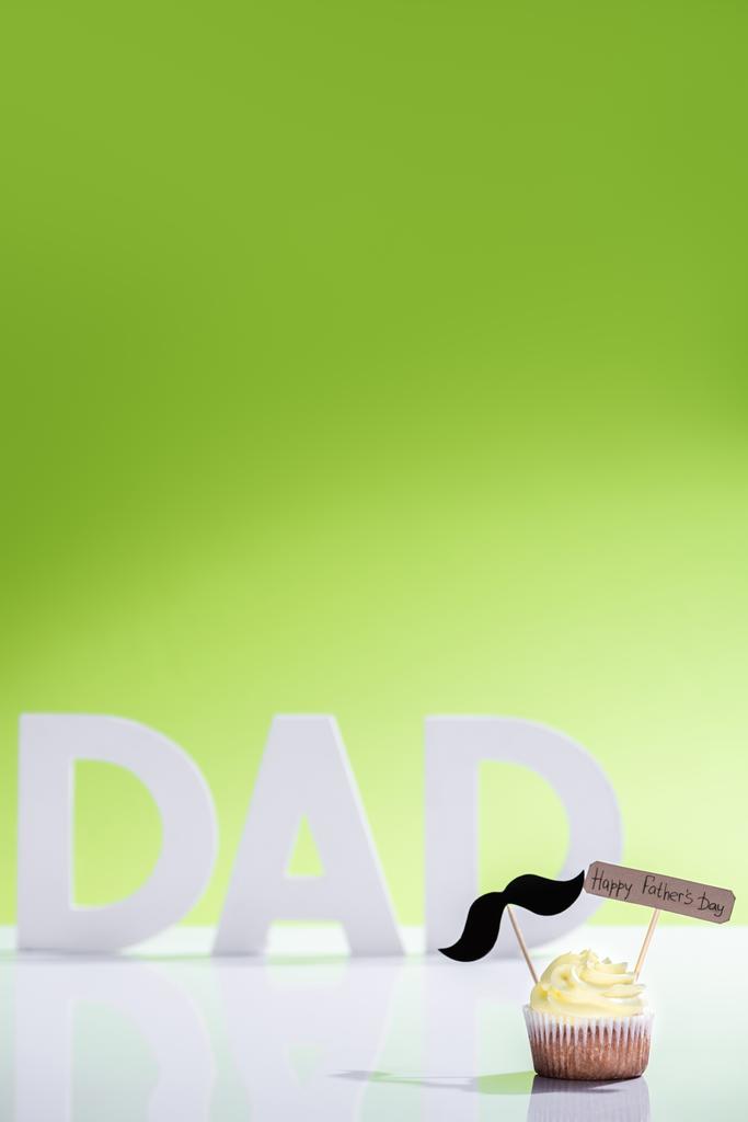 Cupcake με μουστάκι υπογράφουν και ευτυχισμένος πατέρες ημέρα επιγραφή μπροστά ο μπαμπάς επιγραφή κατασκευασμένη από άσπρα γράμματα σε πράσινο - Φωτογραφία, εικόνα
