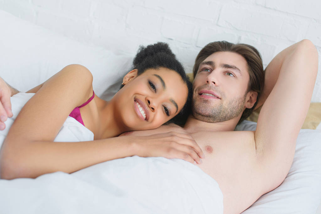 portrét mladé usmívající se pár interracial ležící v posteli a ráno doma - Fotografie, Obrázek