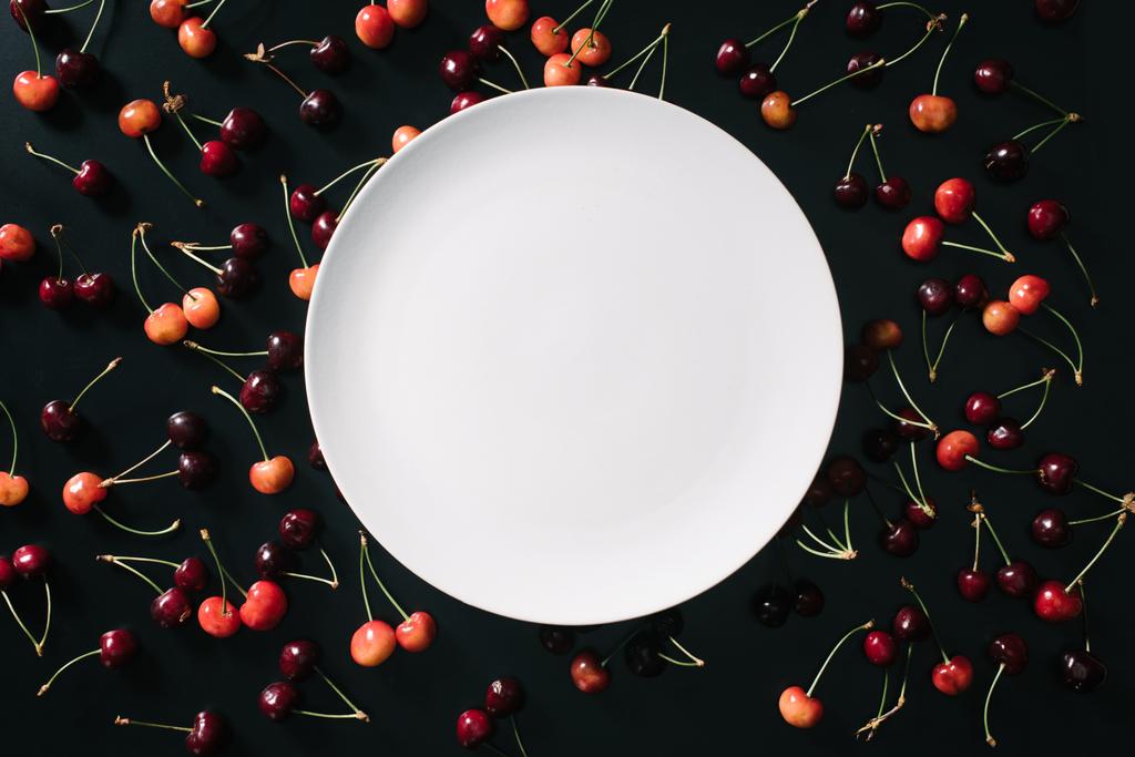 top view of empty round white plate and sweet cherries on black  - Photo, Image