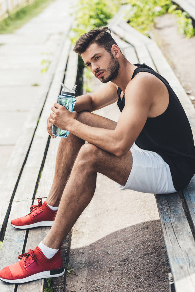 jeune sportif avec bouteille d'eau assis sur un banc à l'aire de jeux sportive
  - Photo, image
