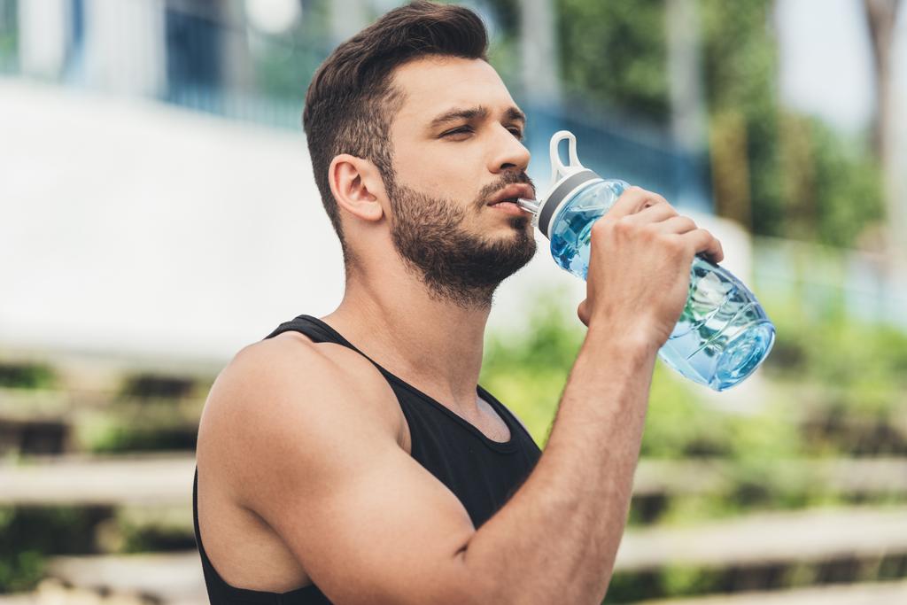 vista lateral del joven deportista bebiendo agua de la botella
  - Foto, imagen
