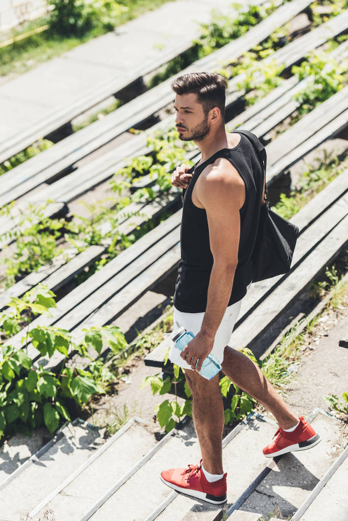 sportovec drží láhev vody a tašky na sportovní vybavení na schodech na sportovní hřiště  - Fotografie, Obrázek