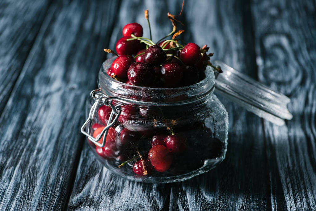 close-up view of ripe sweet healthy cherries in glass jar on wooden table - Photo, Image