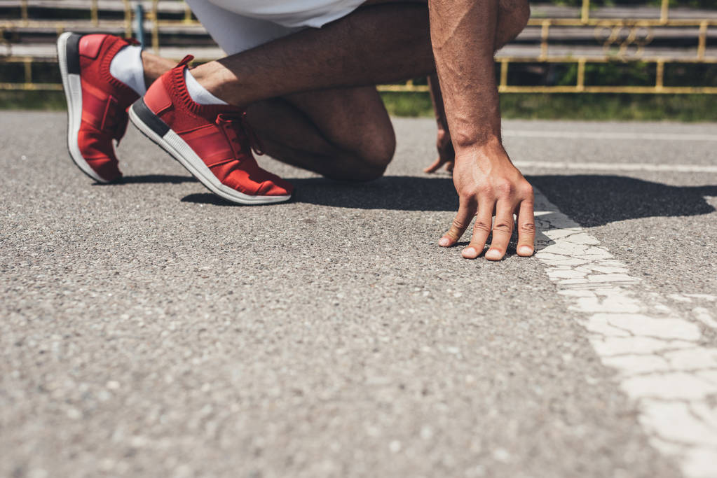 Ausschnittbild eines männlichen Sprinters in Startposition auf Laufstrecke  - Foto, Bild