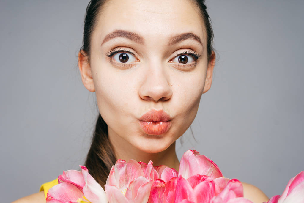 Funny krásná mladá dívka drží růžové květy, při pohledu na fotoaparát a pózování - Fotografie, Obrázek