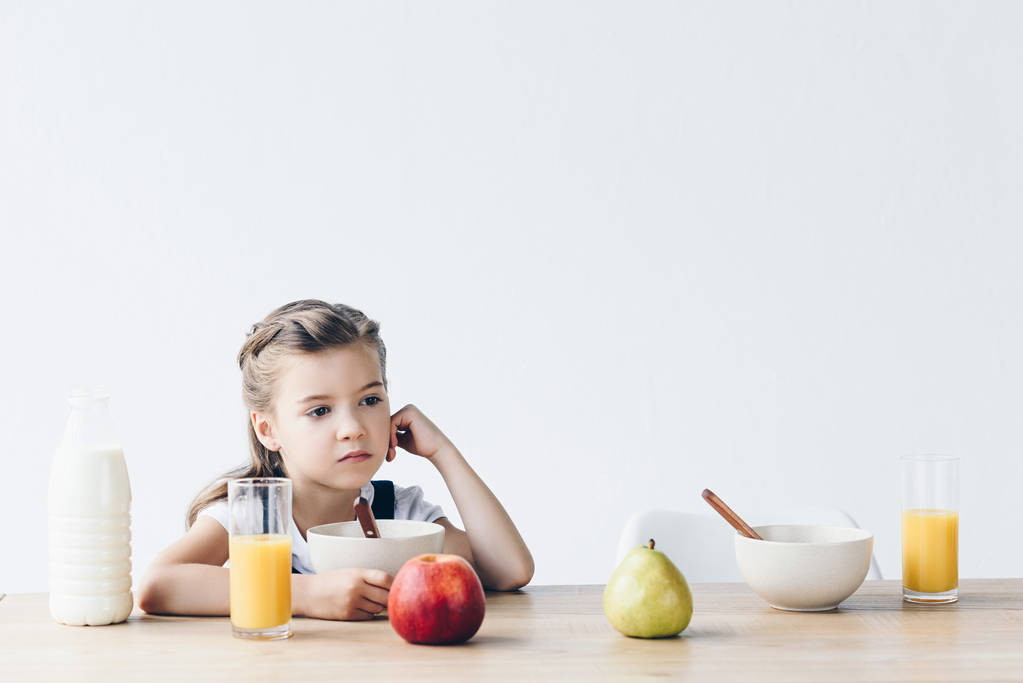 самотня маленька школярка сидить за столом під час сніданку і дивиться ізольовано на білому
 - Фото, зображення
