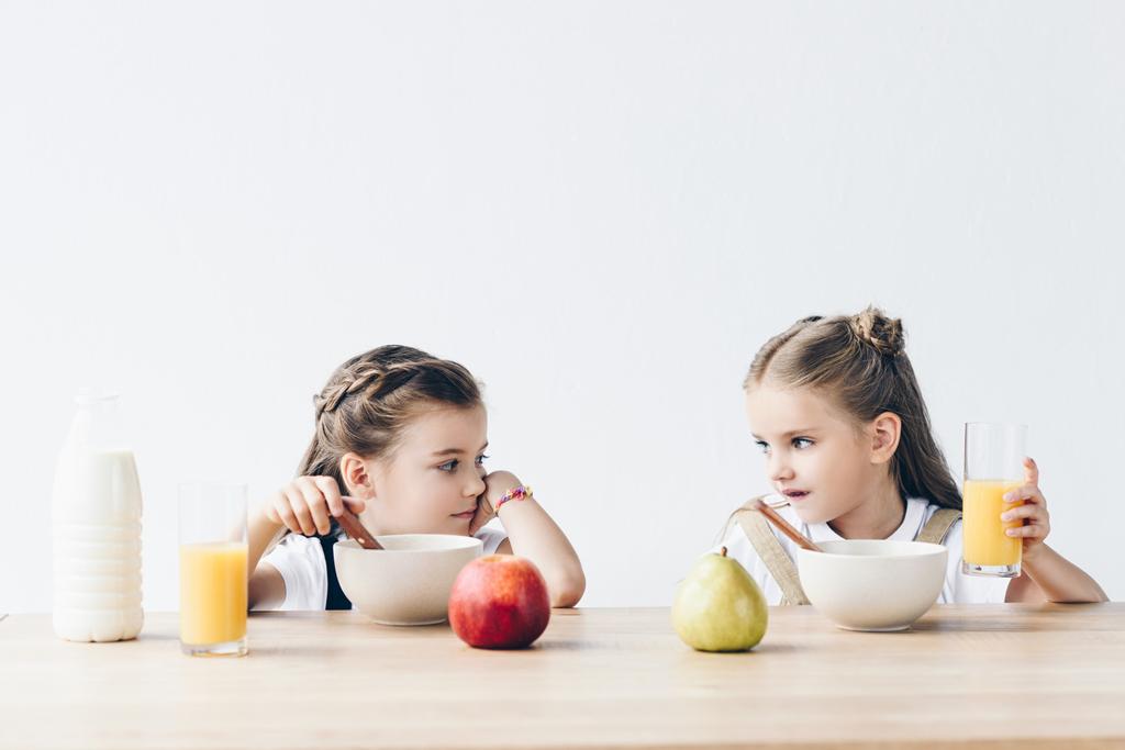 tristi scolarette che mangiano cereali con succo d'arancia e frutta e si guardano isolate sul bianco
 - Foto, immagini