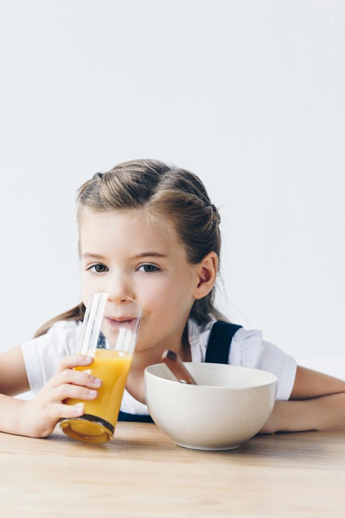 little schoolgirl drinking orange juice during breakfast and looking at camera isolated on white - Photo, Image