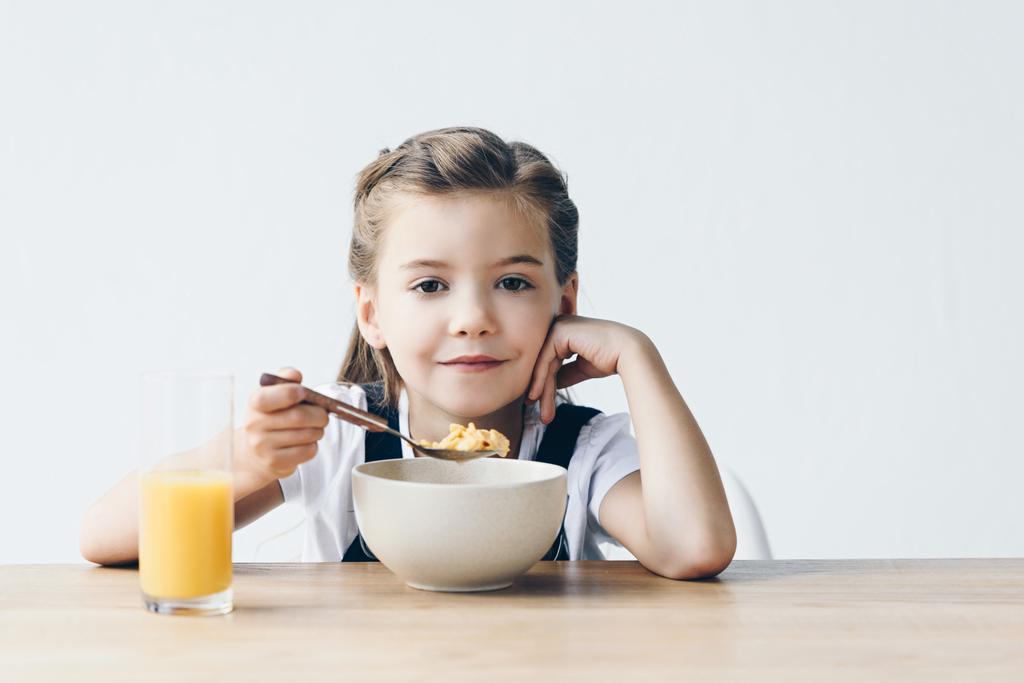 усміхнена маленька школярка їсть здоровий сніданок ізольовано на білому
 - Фото, зображення
