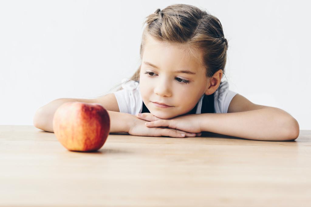 pequena estudante sentada à mesa com maçã vermelha isolada no branco
 - Foto, Imagem