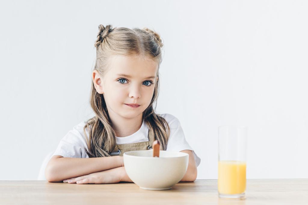 vertrouwen weinig schoolmeisje zit aan tafel met ontbijt geïsoleerd op wit - Foto, afbeelding