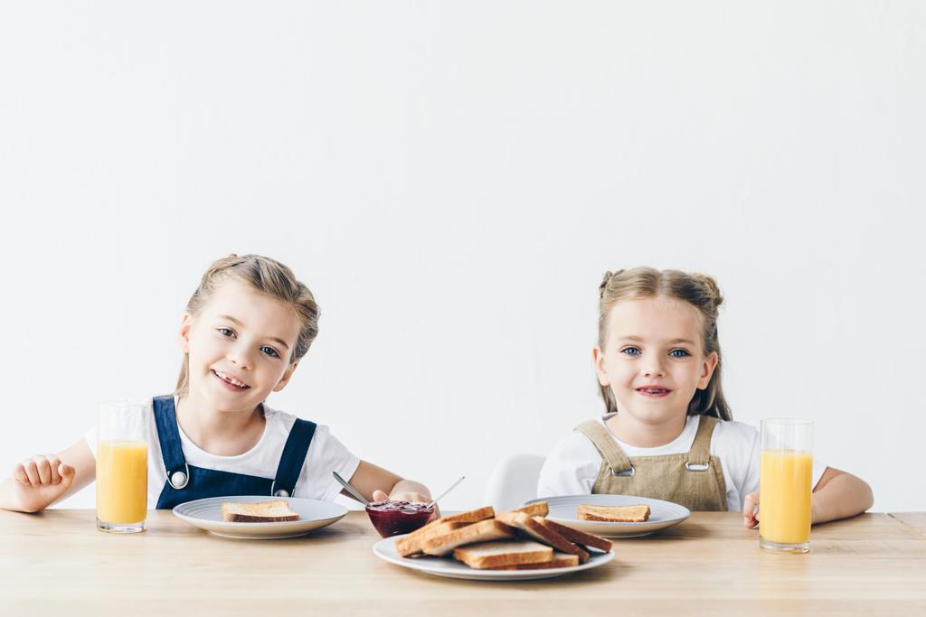 kleine Schwestern, die Toasts mit Marmelade zum Frühstück essen und isoliert auf weiß in die Kamera schauen - Foto, Bild