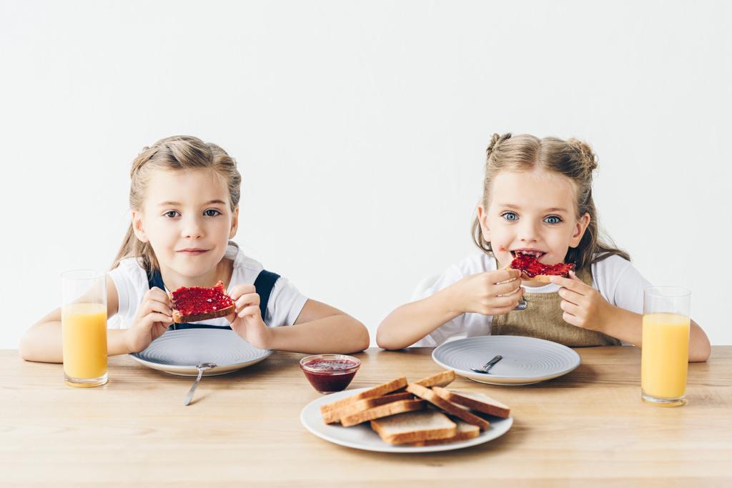 zusjes eten toast met jam bij het ontbijt op wit wordt geïsoleerd - Foto, afbeelding