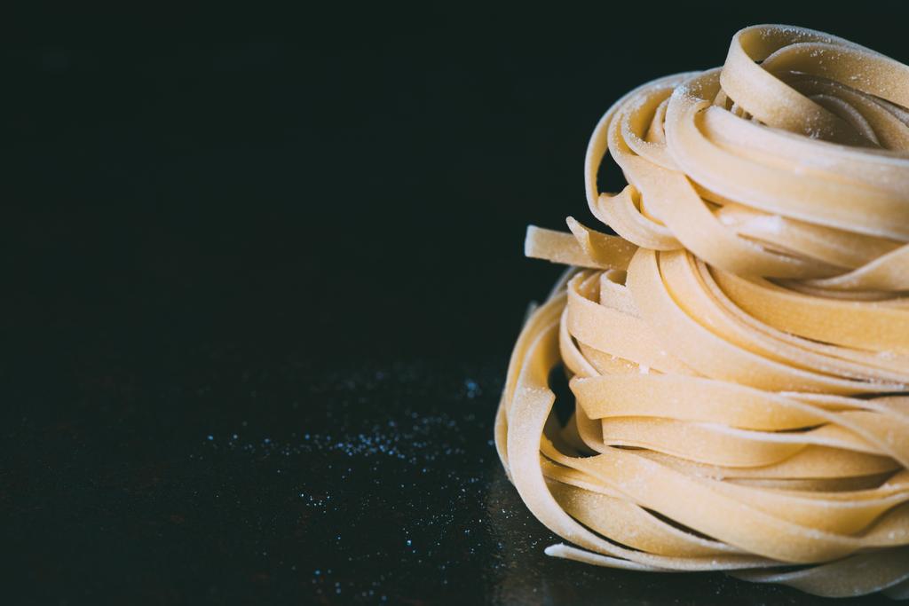 lähikuva raaka tagliatelle pasta kattaa jauhot mustalla pohjalla
  - Valokuva, kuva