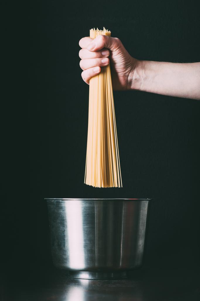 imagen recortada del hombre poniendo espaguetis en la cacerola sobre fondo negro
  - Foto, Imagen